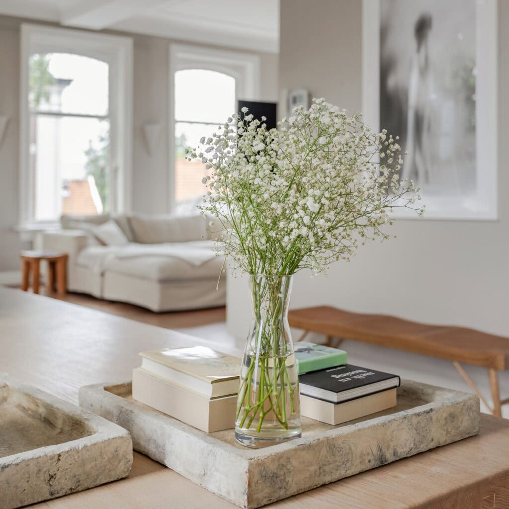 Glass vase on a marble tray with books on a wooden table. In the distance, you can see the sofa.