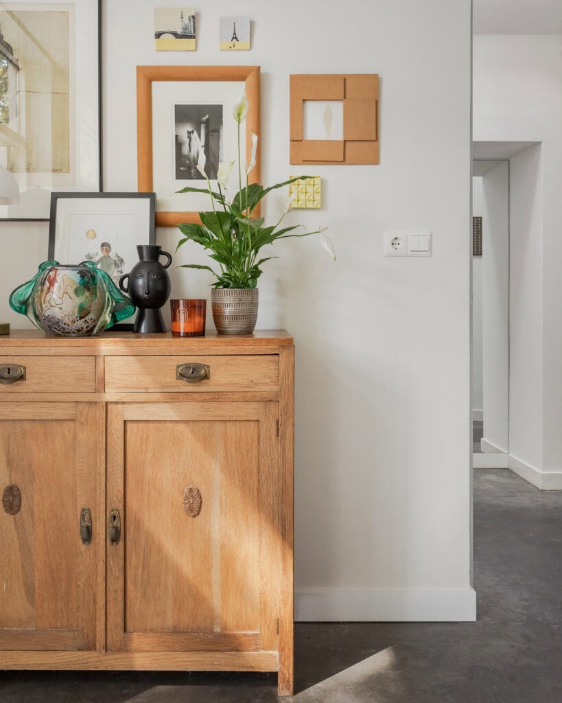 An interior photo of a wooden cabinet with decorative vases and a green plant, complemented by wall art and photo frames.