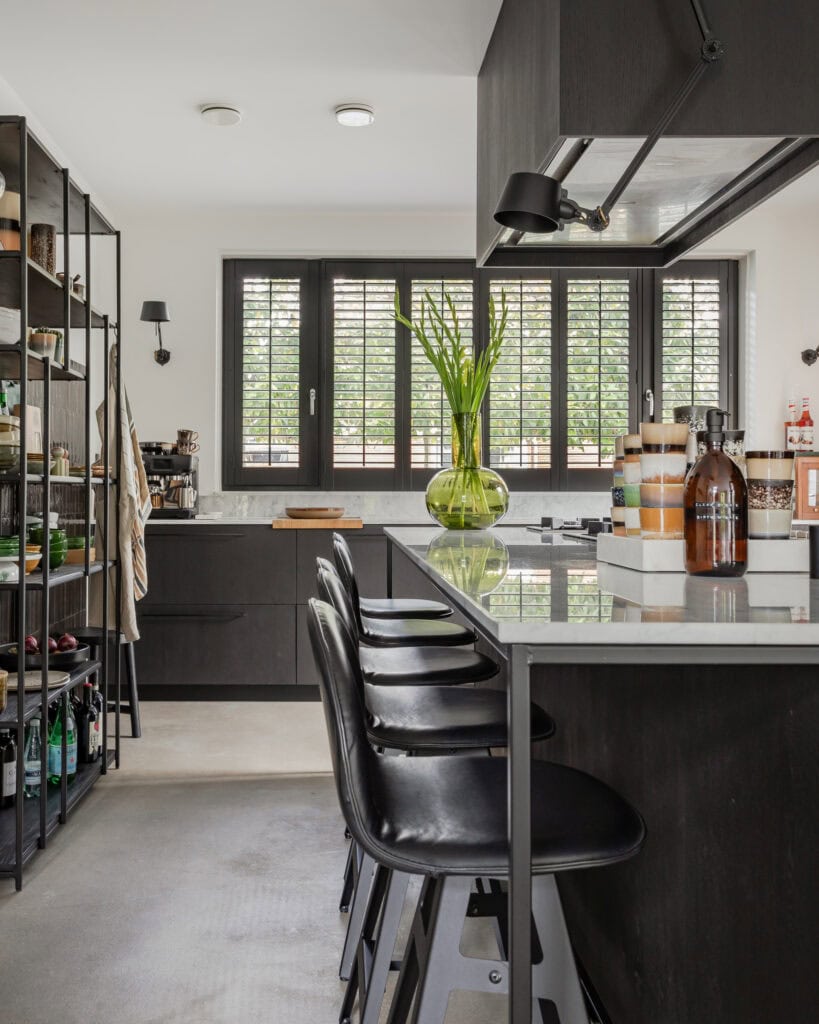 A modern kitchen‑diner with large windows, black furniture and a green vase with flowers.unter.