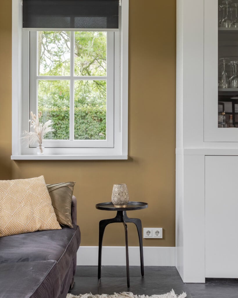 A window with a view of a green garden, in a modern living room with a beige wall and black tiled floor.