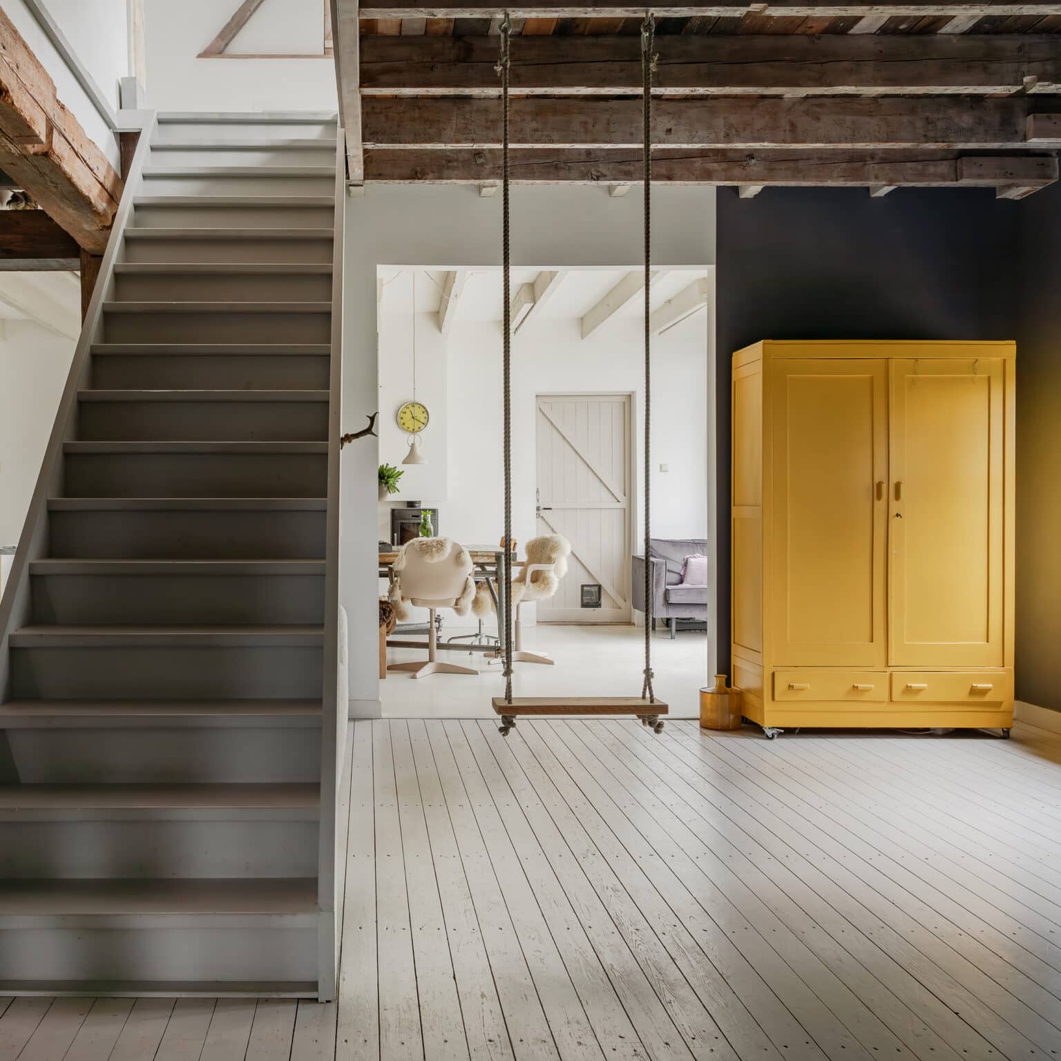 A bright hallway with a bright yellow cabinet, an open staircase, and a view through to the living room.