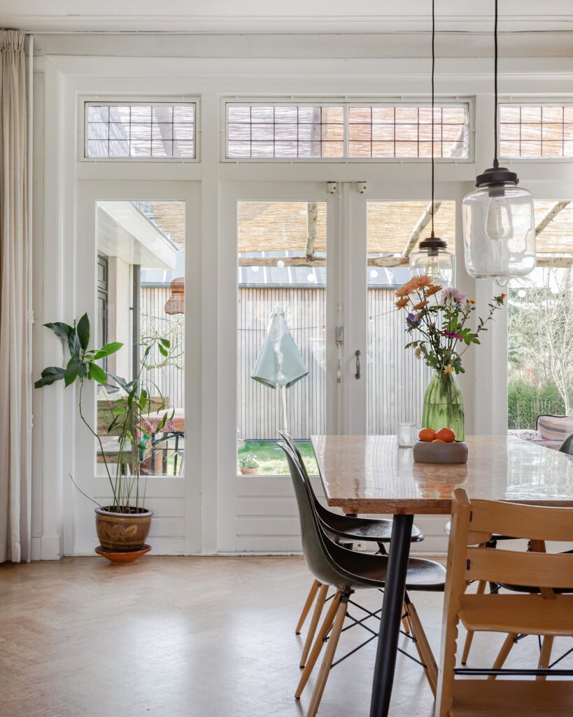 Bright room in a 1930s house with a dining table and designer chairs overlooking the garden.