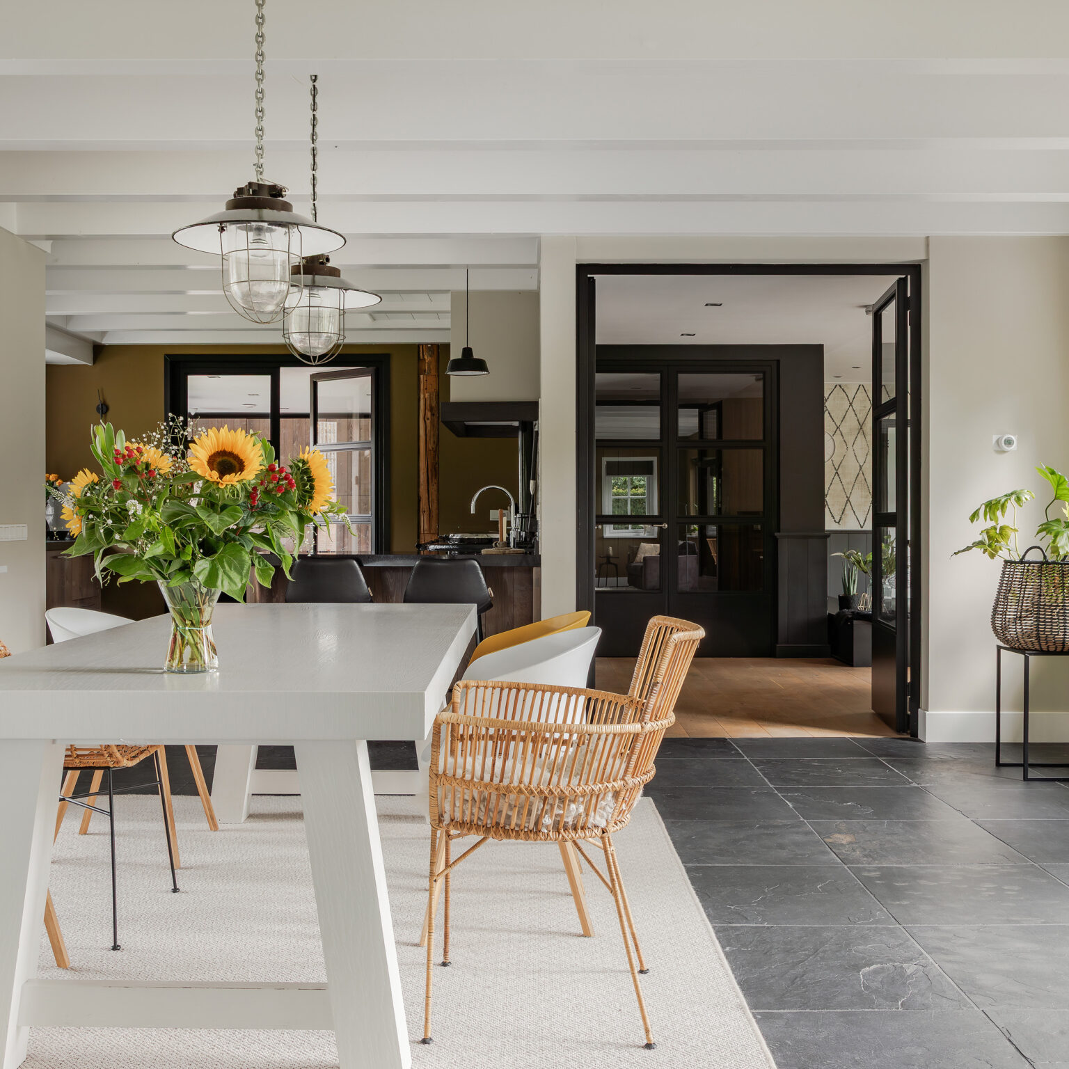 Eetkamer in woonboerderij met witte tafel en verschillende stoelen. Op de achtergrond de keuken en de woonkamer.