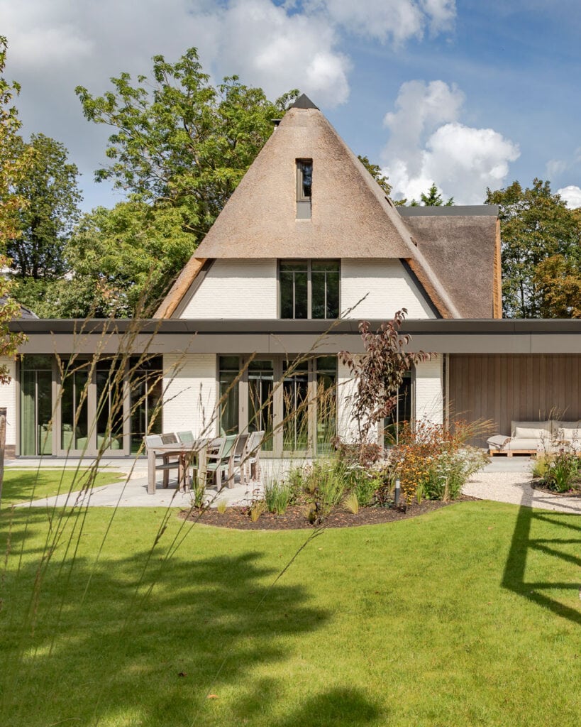 Thatched-roof villa with a lawn in the foreground and trees in the background.