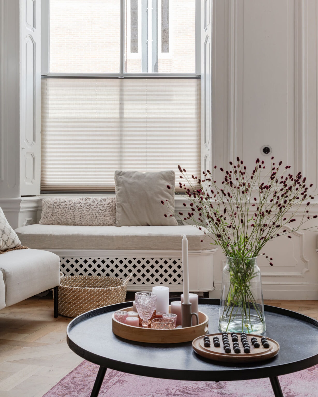 Een lichte woonkamer met grote ramen, een bank, bloemen en decoratieve accessoires.