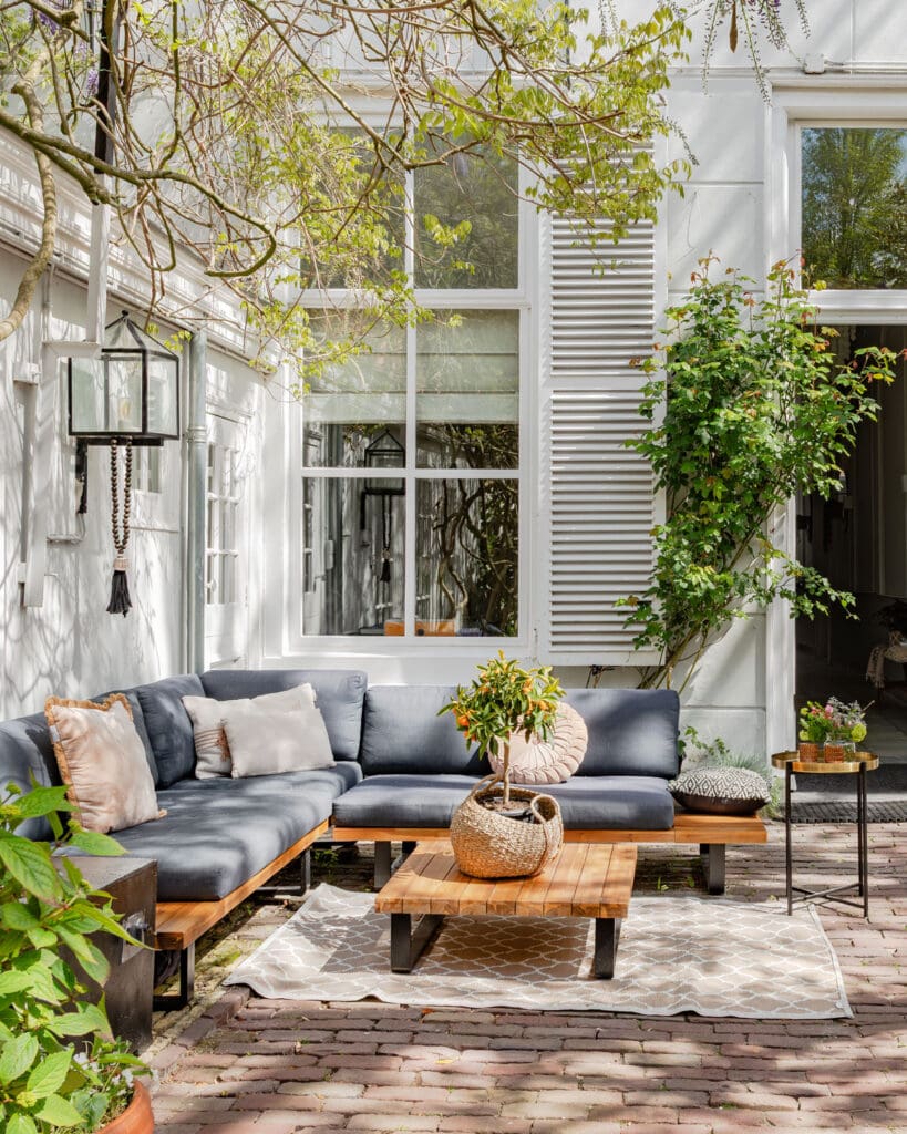 A cozy seating area with an outdoor sofa, plants, and a wooden table in a garden.