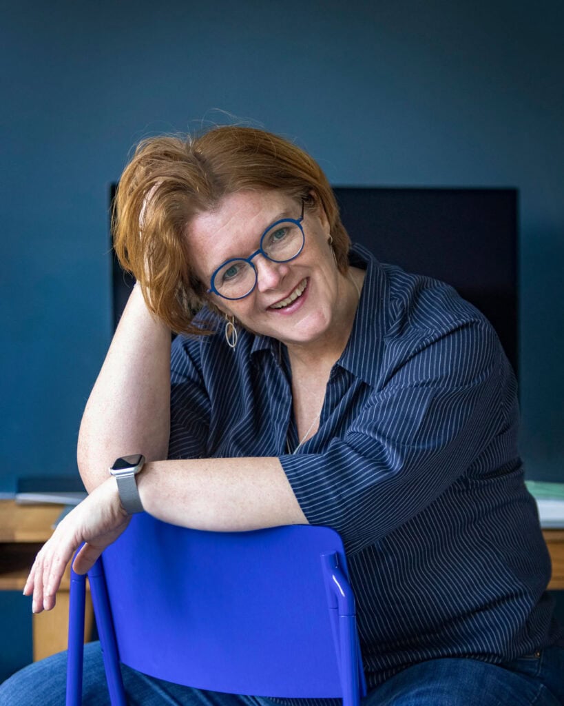 Smiling Nicolet, a woman with red hair and blue glasses in an office.
