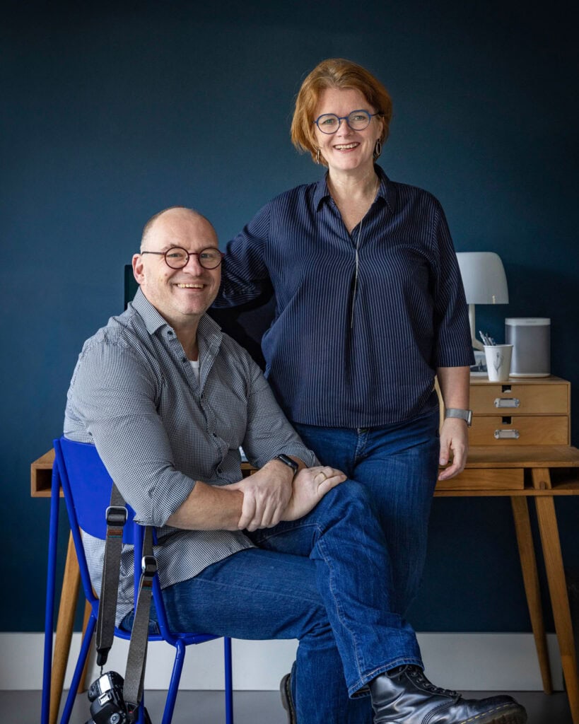 Two people, Guillaume and Nicolet, are smiling and posing in a modern office environment with a blue background.