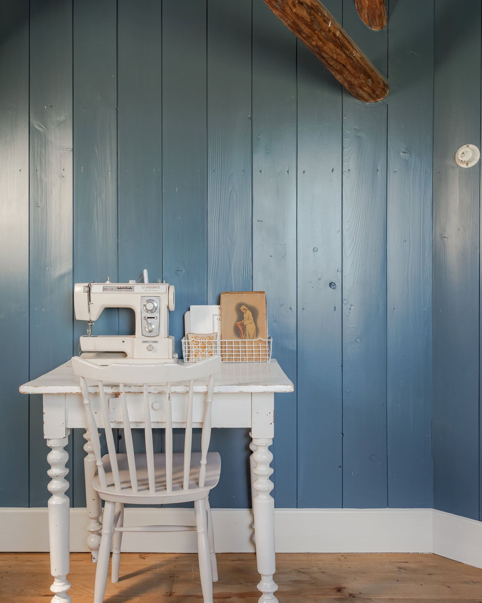 Interior photography: A vintage wooden table with a sewing machine against a blue wall of wooden panels