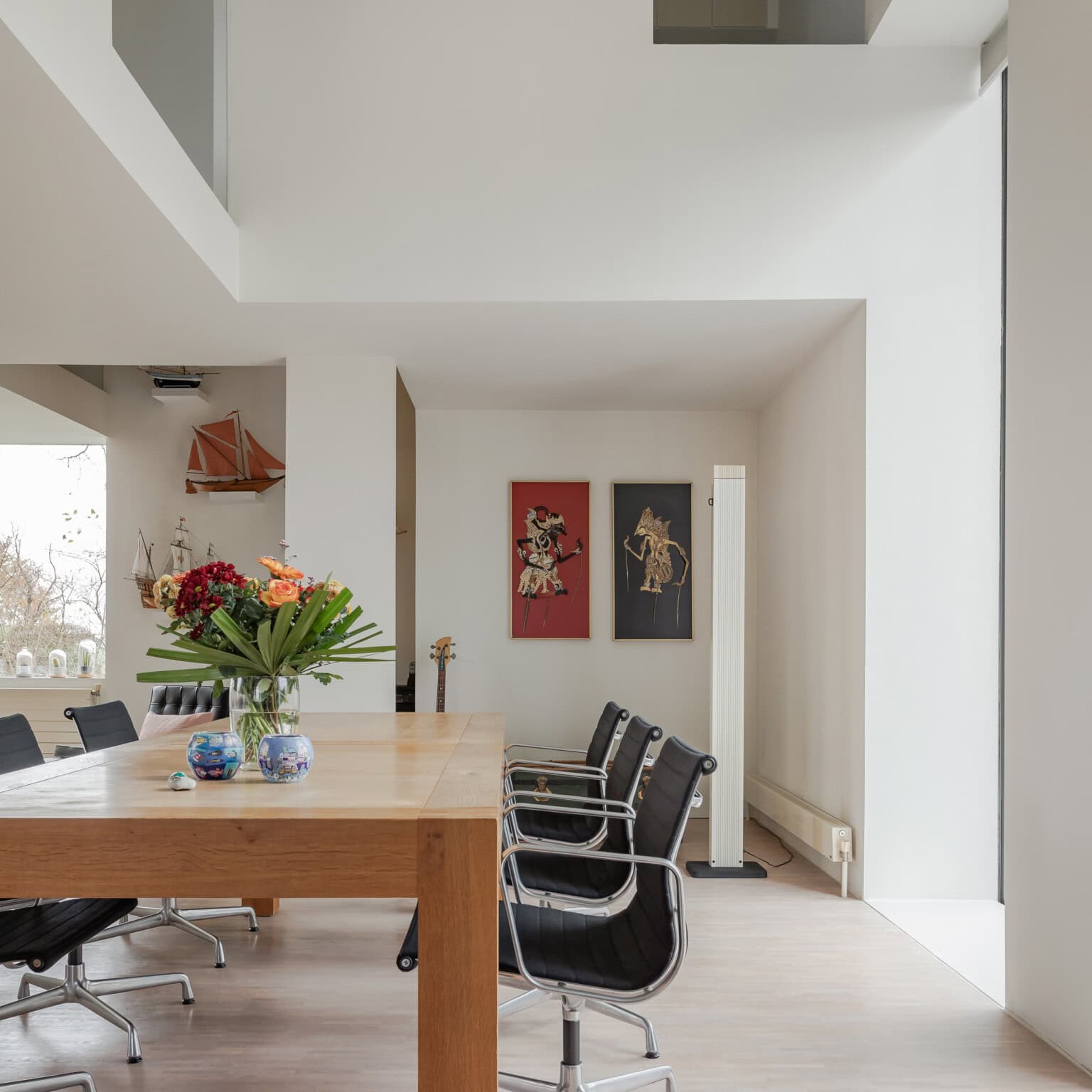 Diningroom with bright white walls a high ceiling and designers chairs.