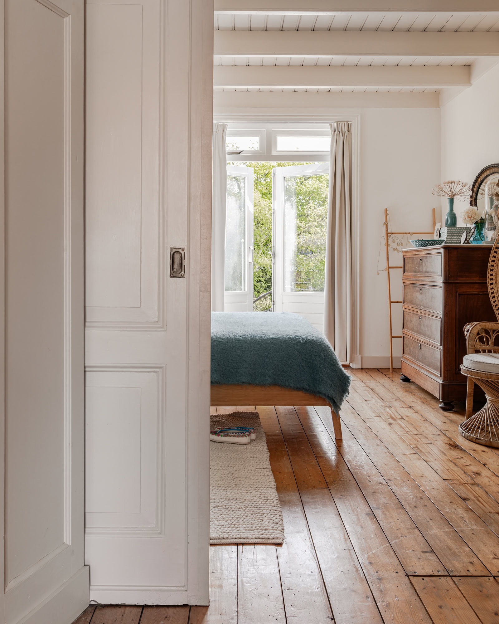 A view through to a bedroom with ensuite doors. Vintage furniture and a blue throw on the bed.