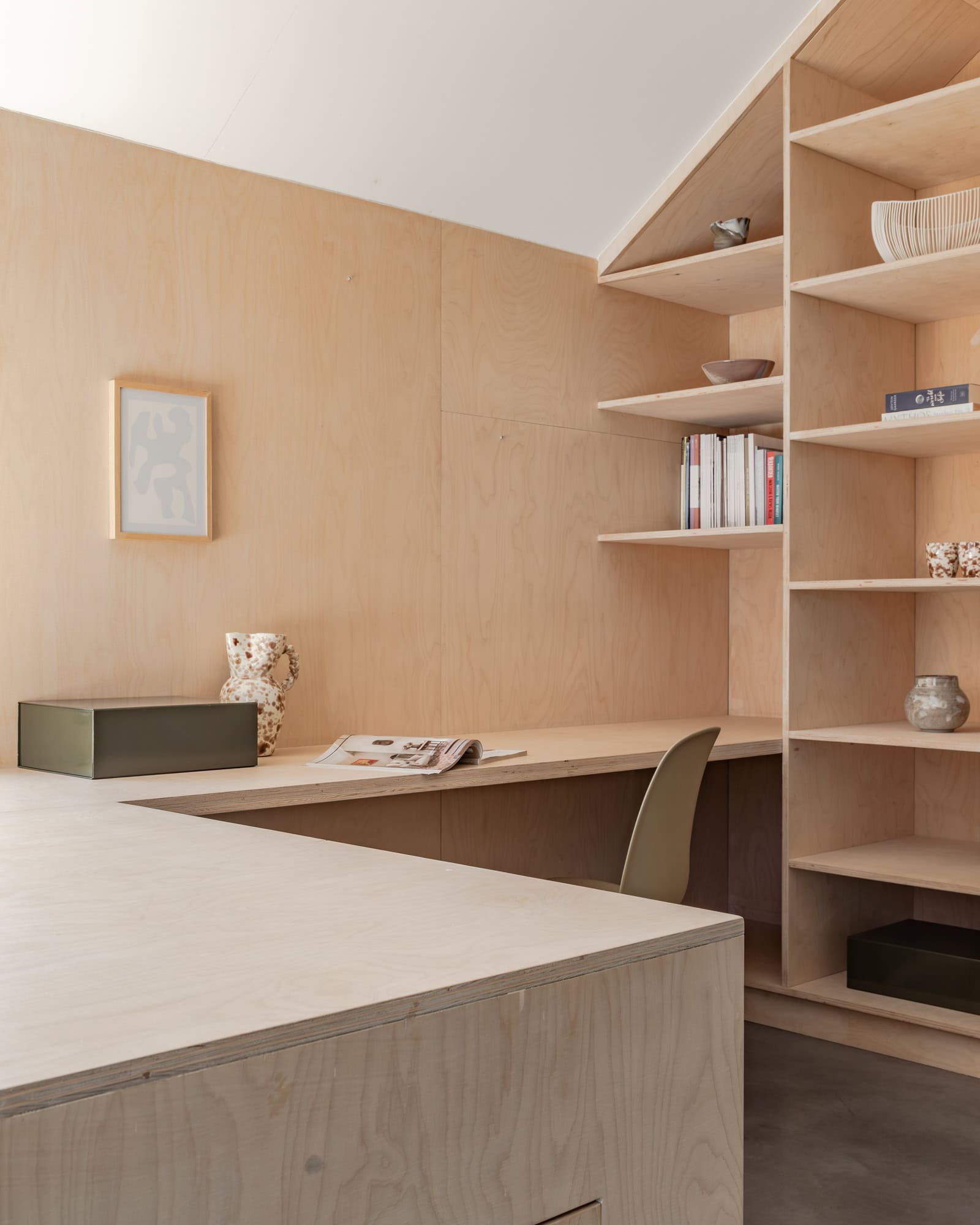 A workspace in a bedroom with built-in plywood furniture and green accents.