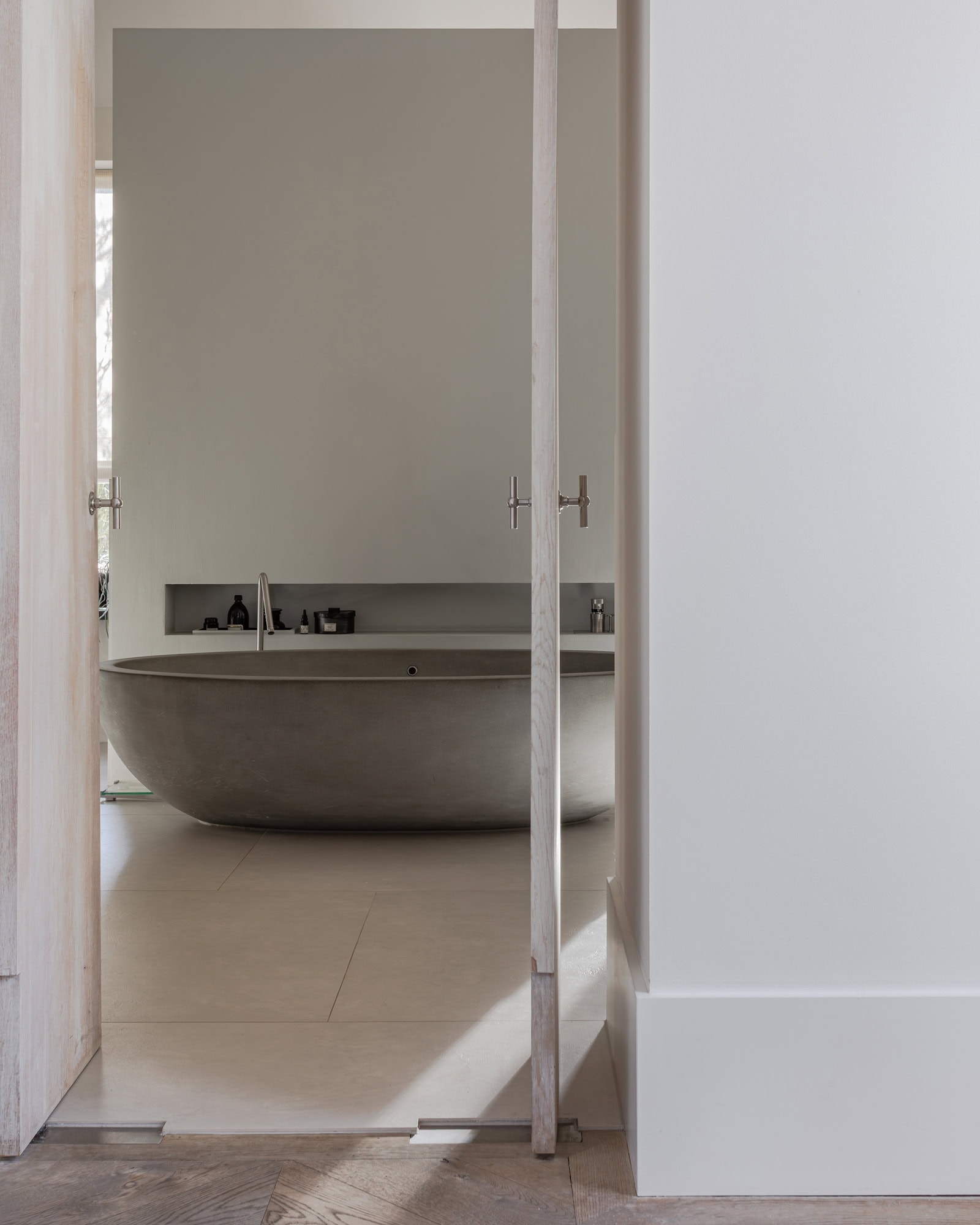 A view through to a bathroom with double doors and an oval concrete bathtub.