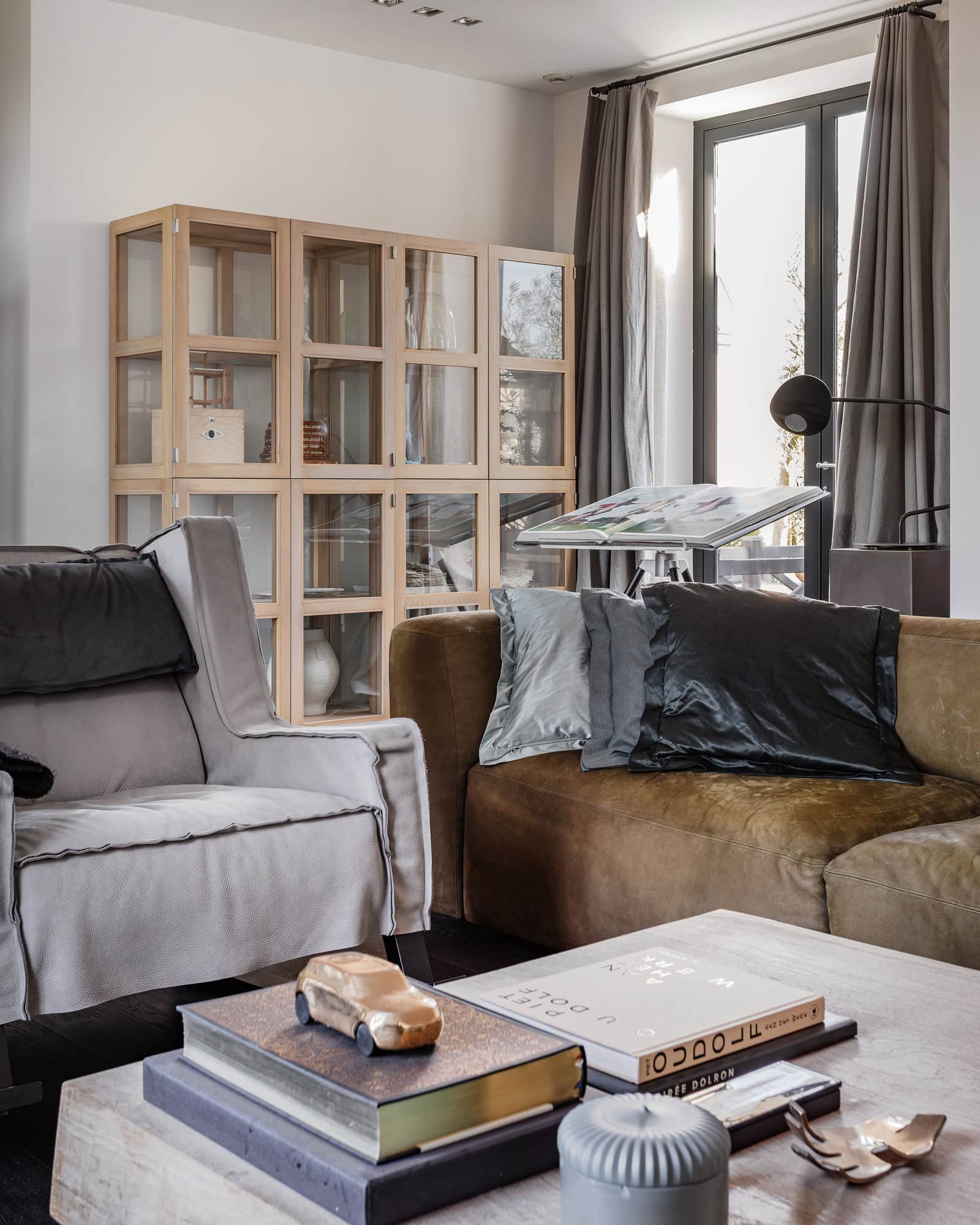 A living room with a sofa and armchair in the foreground and a wooden display cabinet in the background. Everything in natural tones.