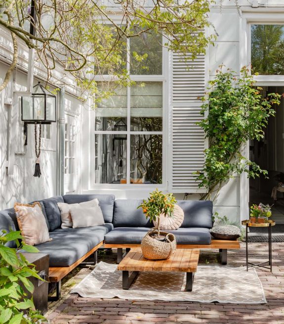 Een gezellige zithoek met buitenbank, planten en houten tafel in een tuin. Fotografie door Nicolet Groen